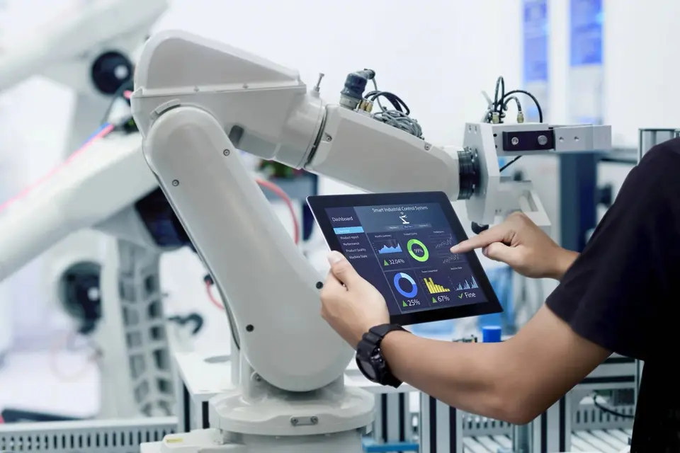 Engineer using a tablet dashboard to monitor an IoT-connected robotic arm